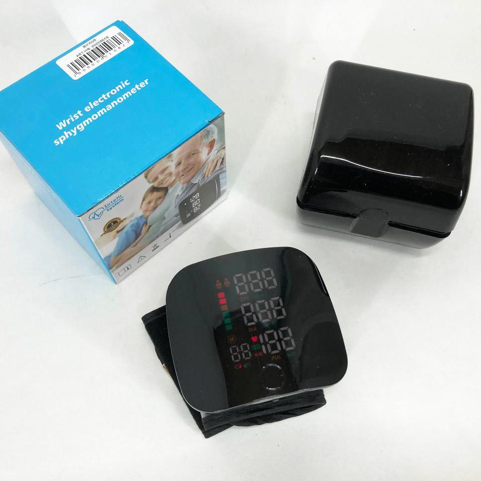 Tensiómetro digital de muñeca negro con pantalla encendida, junto a su estuche rígido y la caja original